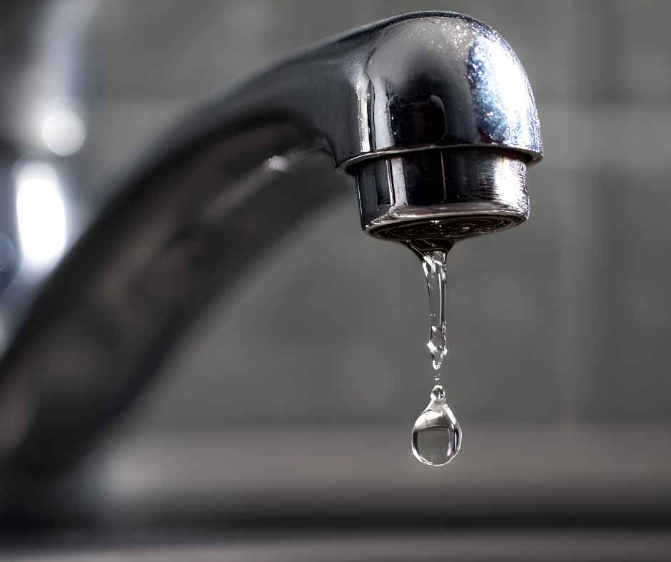 Close-up of a chrome faucet dripping water with a single droplet about to fall.